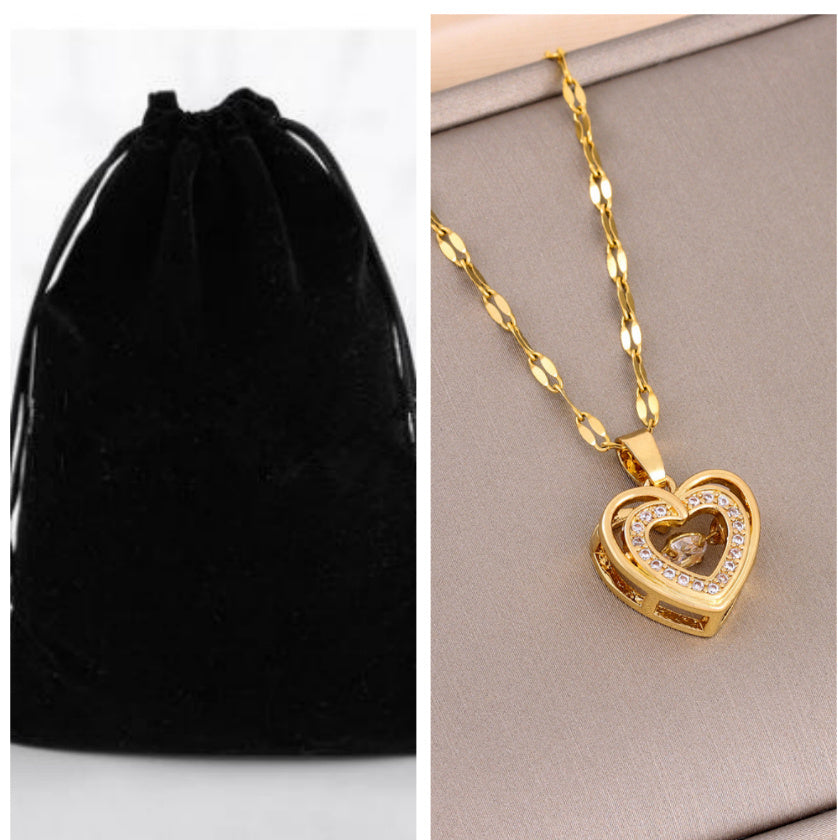 Gold heart-shaped necklace with chain on a gray surface next to a black velvet pouch. women’s necklace with rhinestones