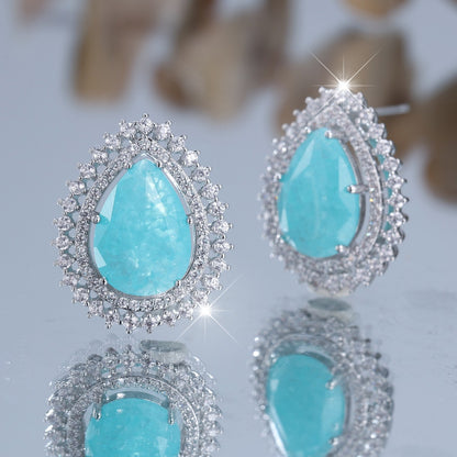 Turquoise teardrop earrings with silver frames on a reflective surface