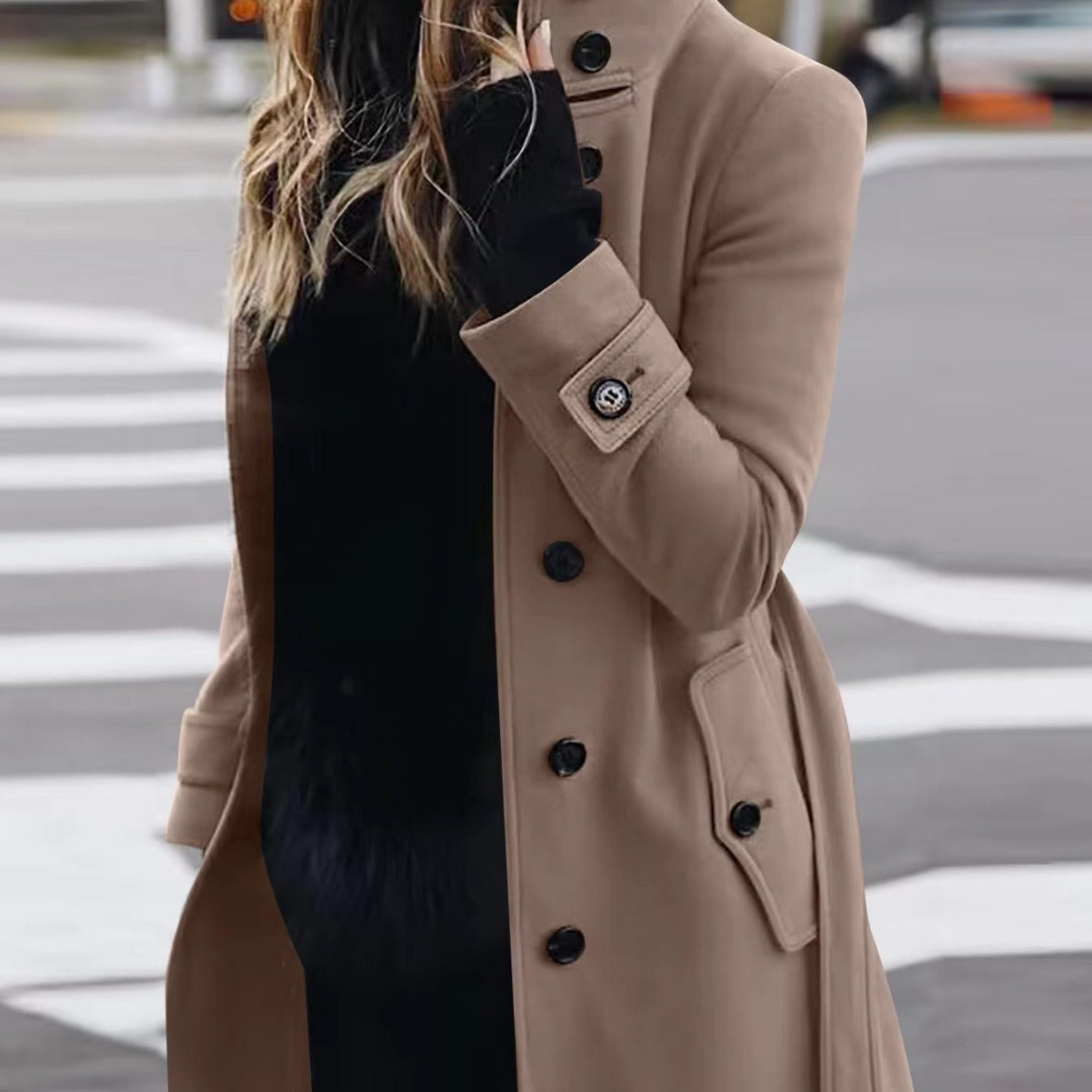 Person wearing a beige trench coat with black buttons on a city street.